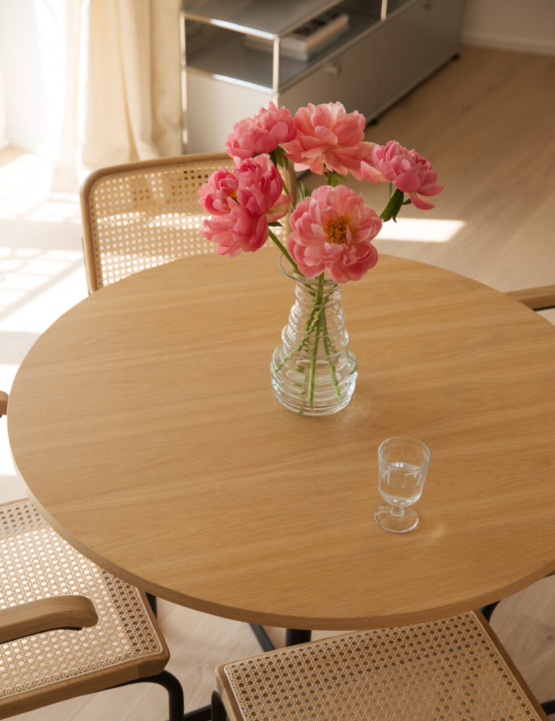 Ein runder Tisch in einem Mietstudio, dekoriert mit einer Vase voller frischer Blumen.